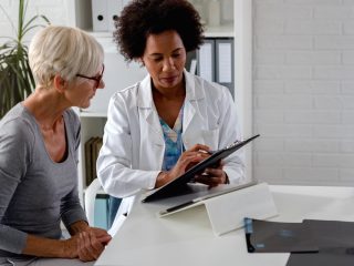 A female doctor sits at her desk and chats to an elderly female patient while looking at her test results A female doctor sits at her desk and chats to an elderly female patient while looking at her test results