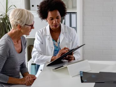 A female doctor sits at her desk and chats to an elderly female patient while looking at her test results A female doctor sits at her desk and chats to an elderly female patient while looking at her test results